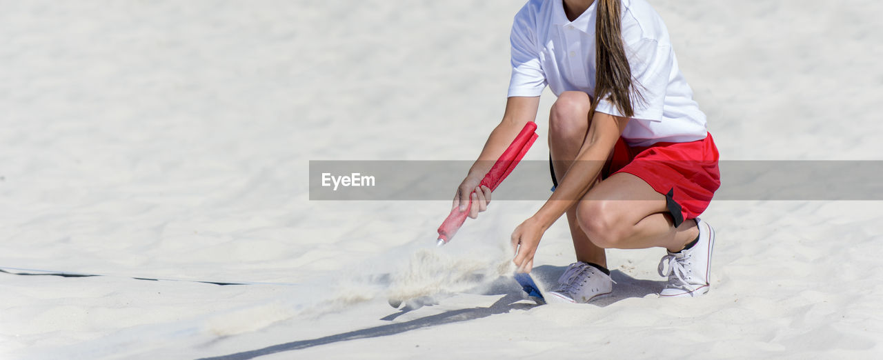 Low section of woman crouching on sand during sunny day