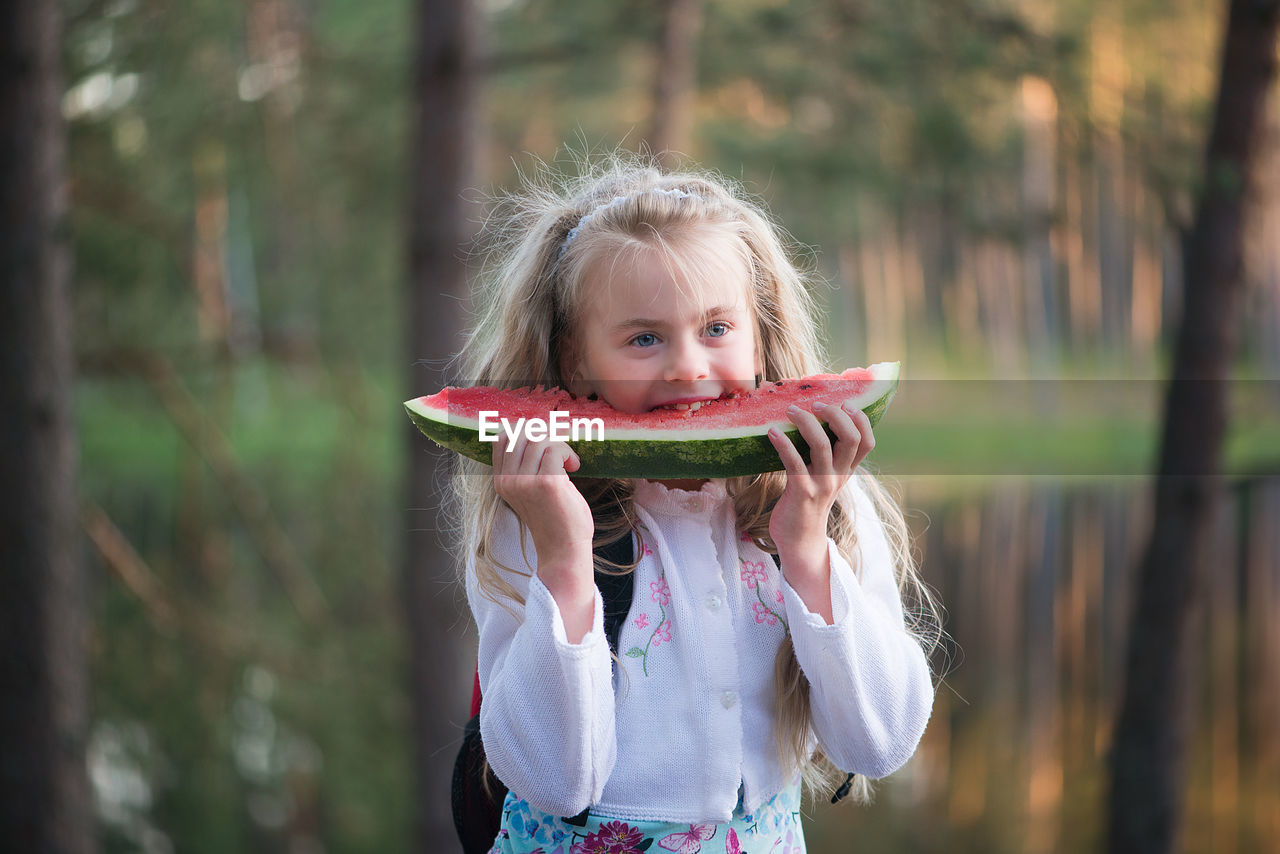 Girl eating watermelon while standing against lake