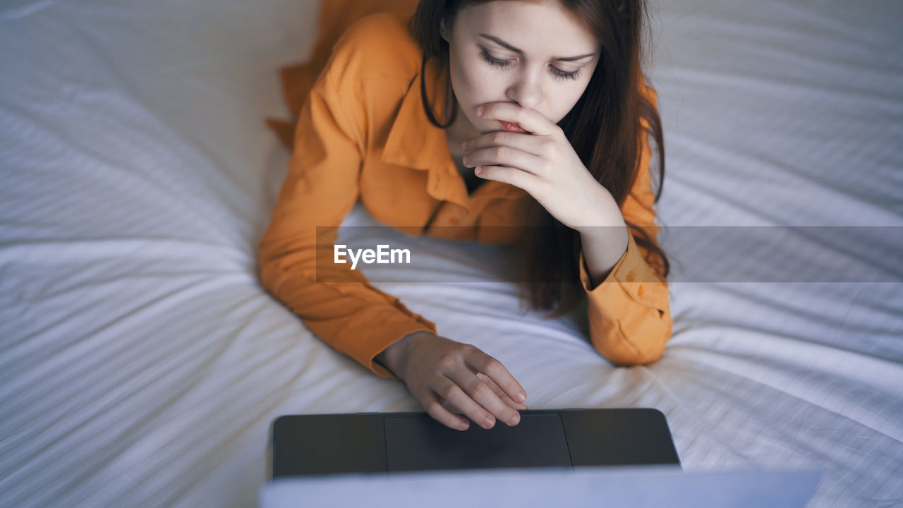 young woman using mobile phone while sitting on bed