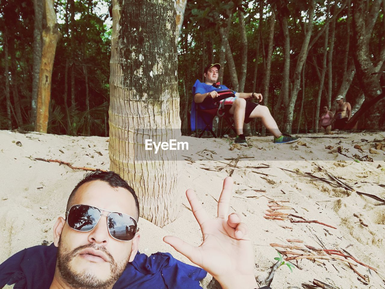 PORTRAIT OF HAPPY FRIENDS SITTING BY TREE IN FOREST