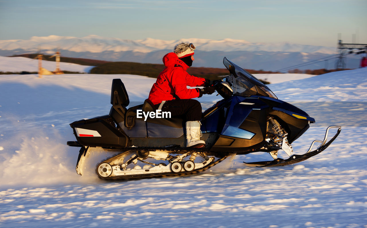 Side view of man riding snowmobile on snow covered landscape