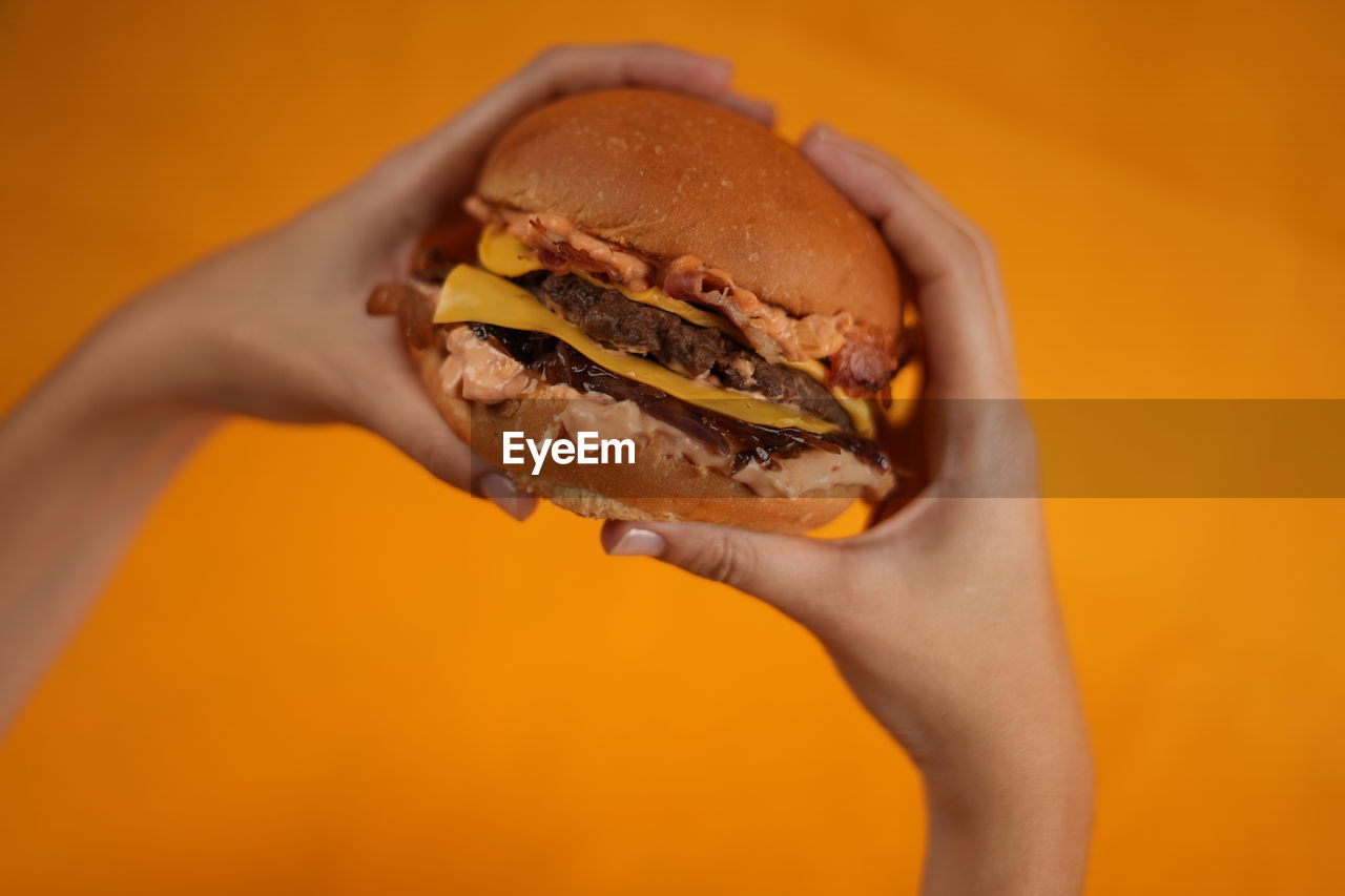
hands of a young man taking a beef burger with cheddar cheese