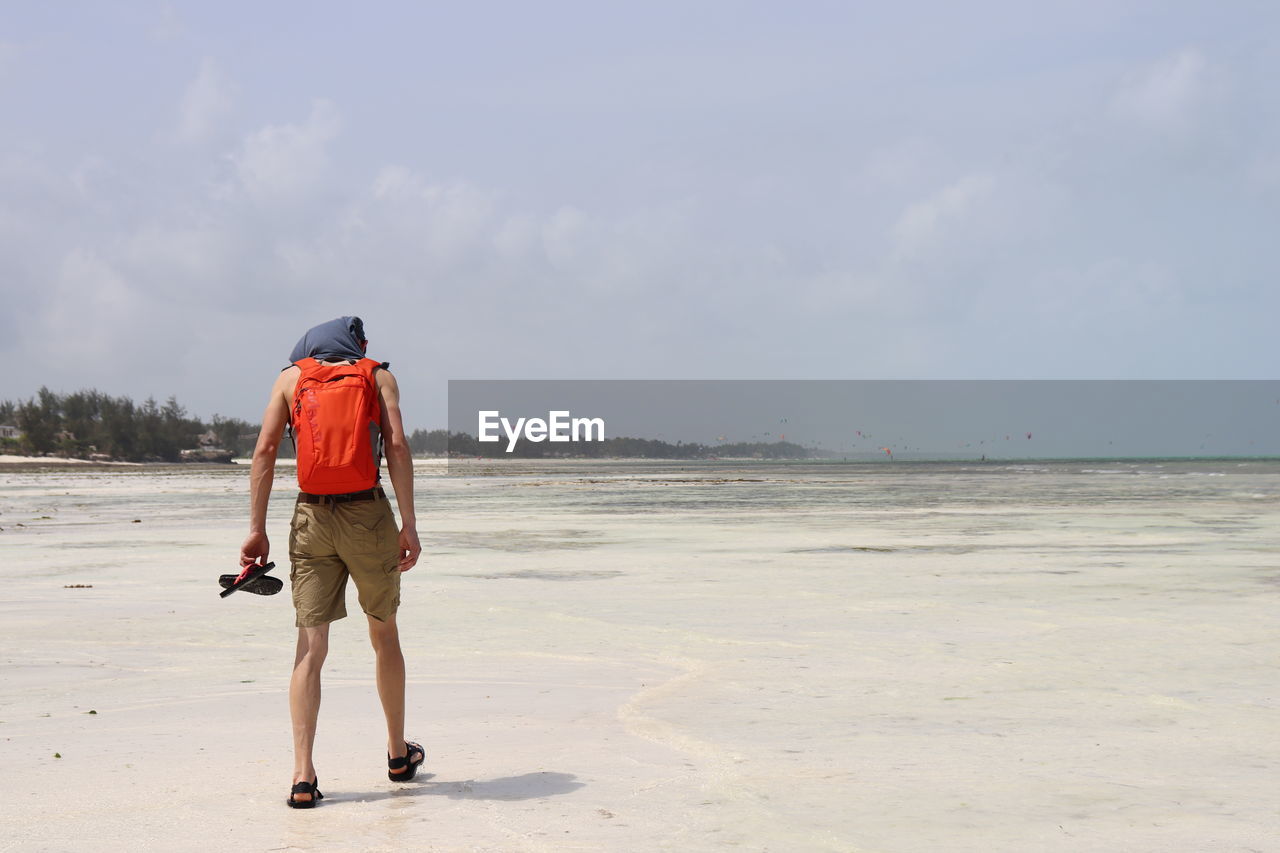 Full length rear view of man walking at beach against sky