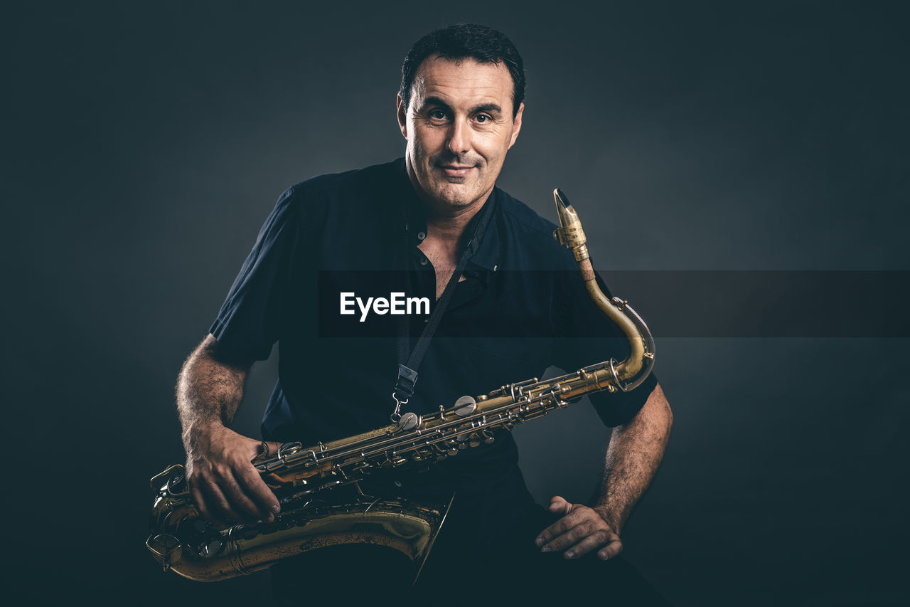 Portrait of mature man holding saxophone against black background