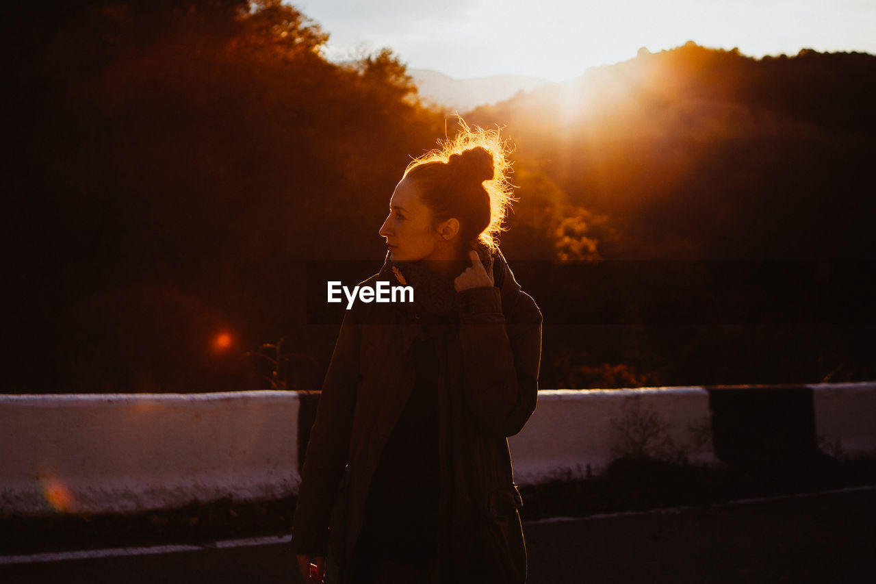 A young woman stands on the road in the bright setting back sun