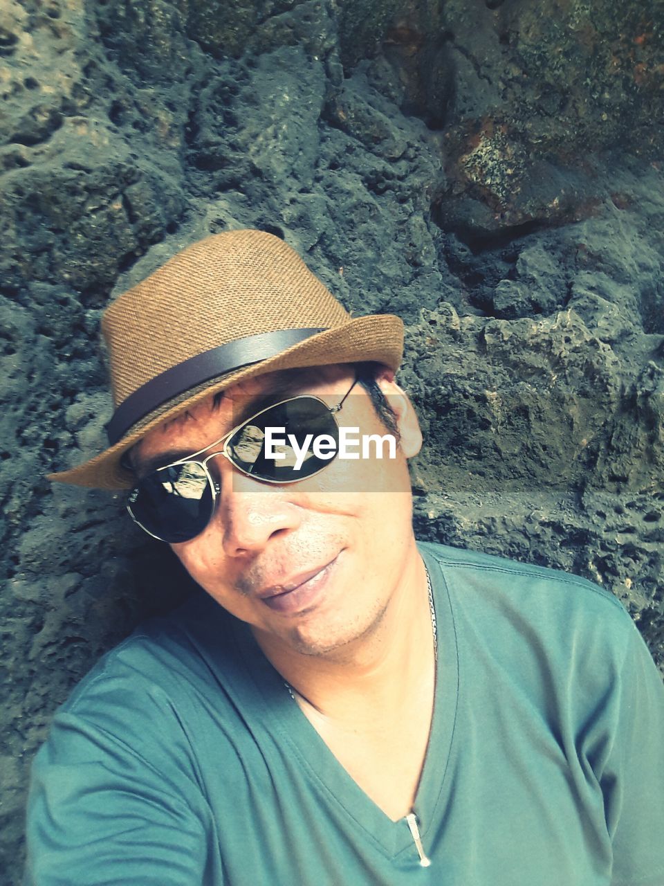Happy man wearing hat and sunglasses against rock formation