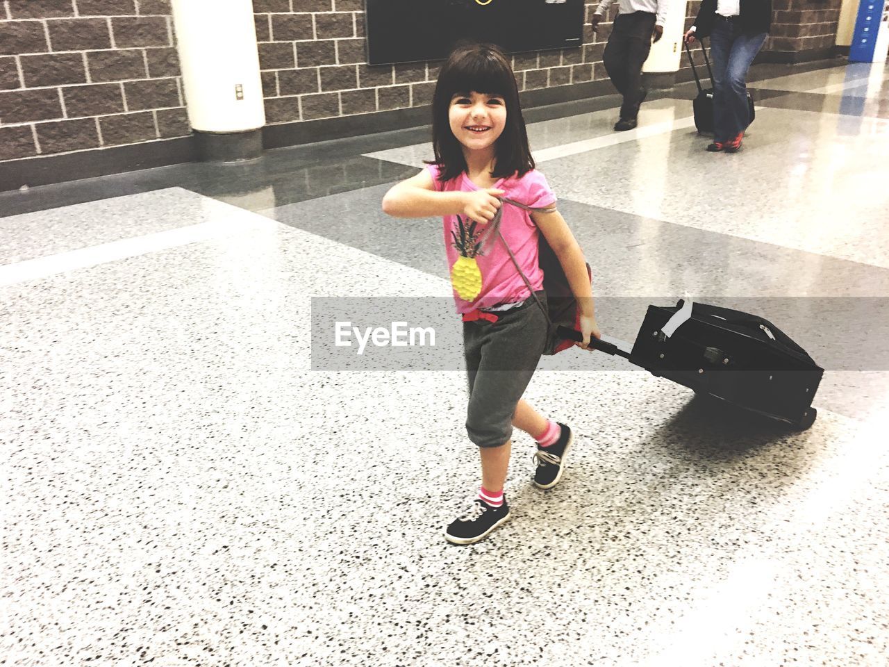 Smiling girl with luggage walking at airport terminal