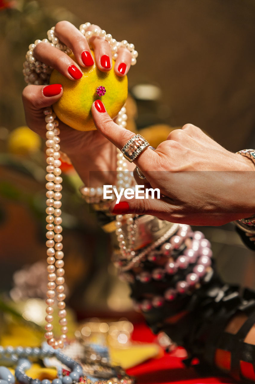 Cropped hands of woman wearing jewelry holding orange