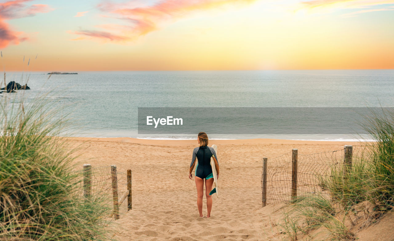 Surfer woman with wetsuit and surfboard looking at the sea