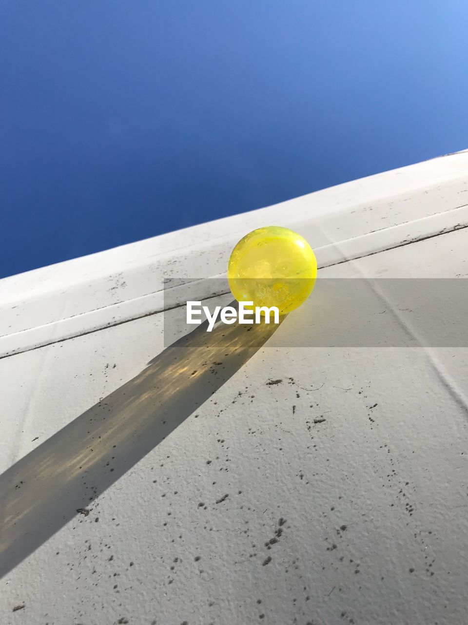 Low angle view of yellow balloon on wall against clear blue sky