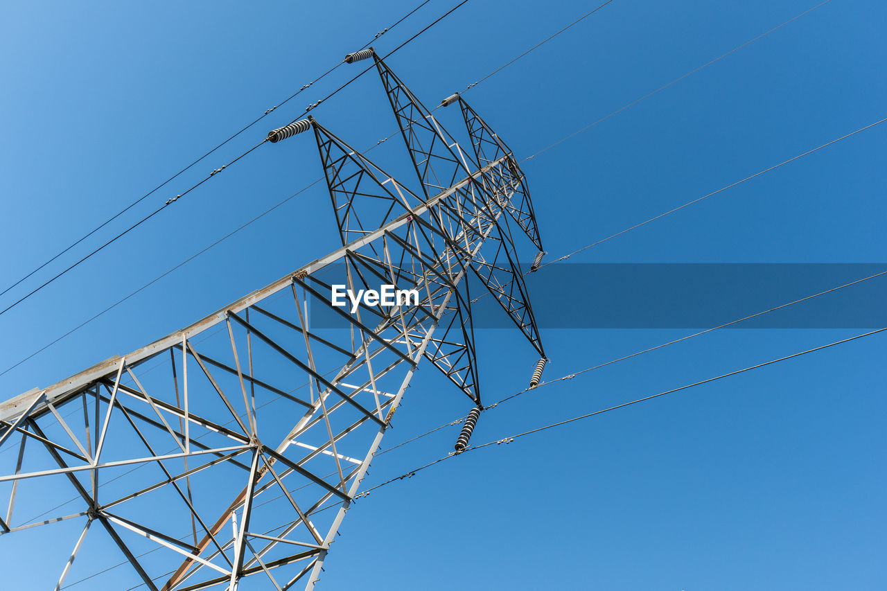 Low angle view of electricity pylon against clear blue sky