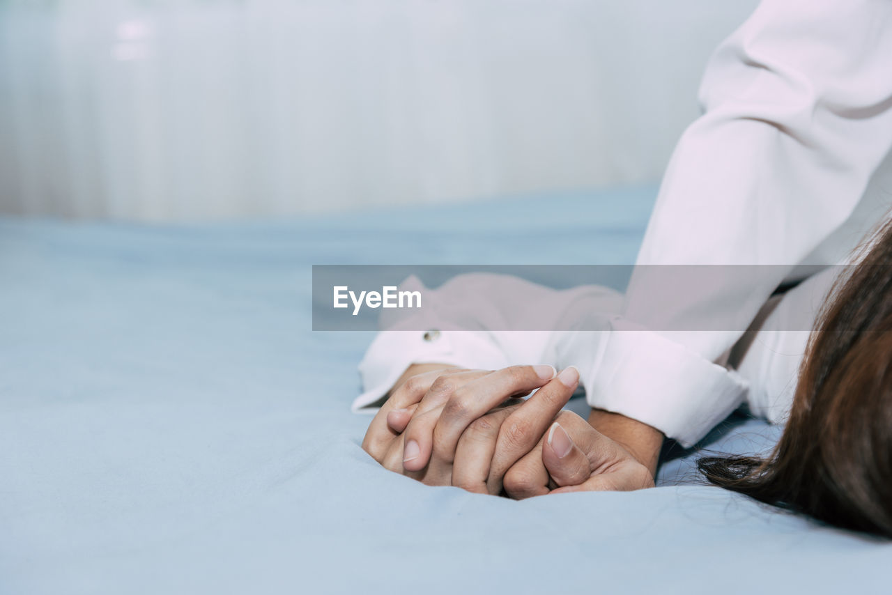 Cropped image of couple holding hands on bed