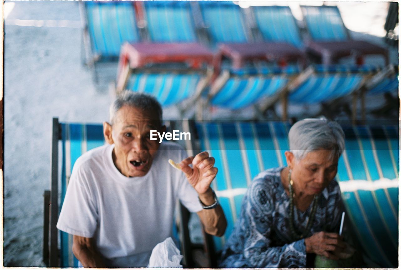 Senior people sitting on deck chair while having food at beach
