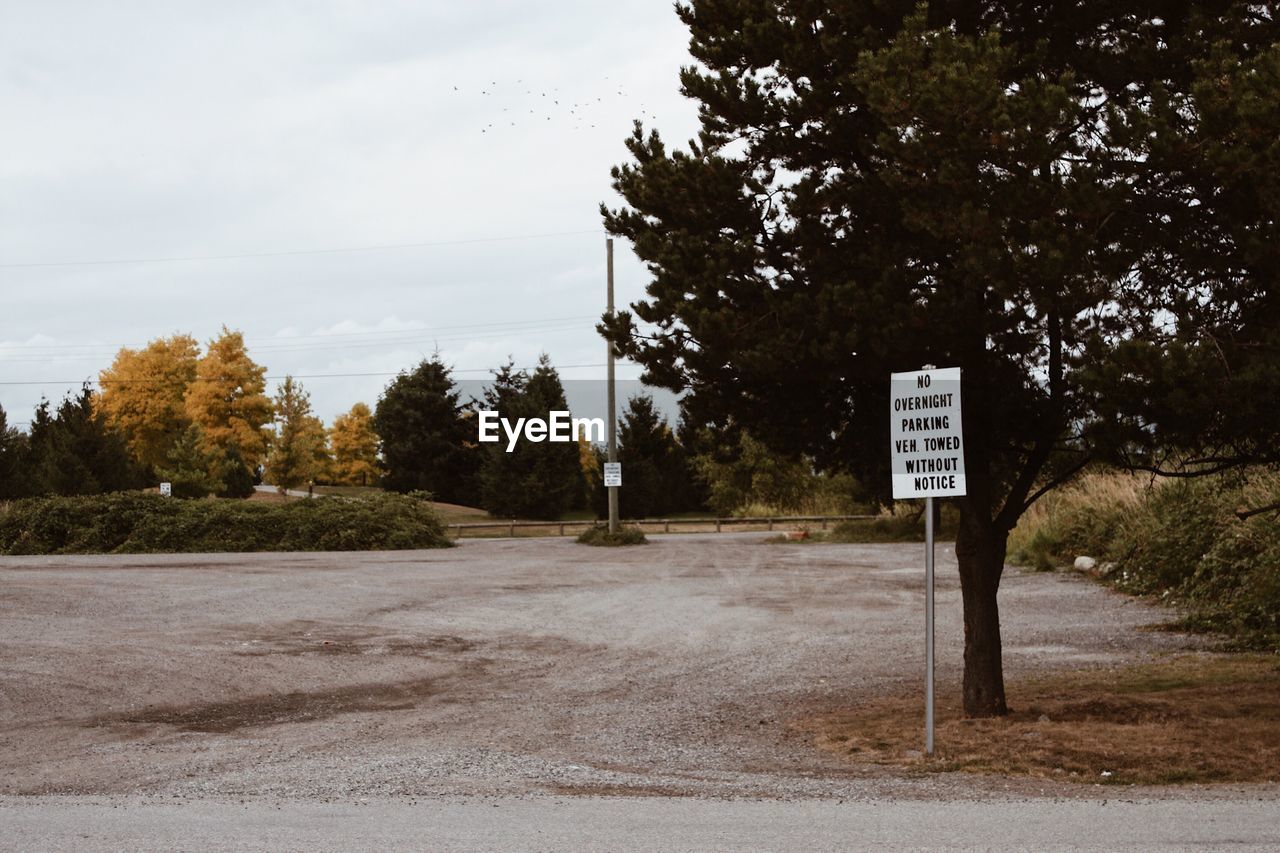 Road sign by trees against sky