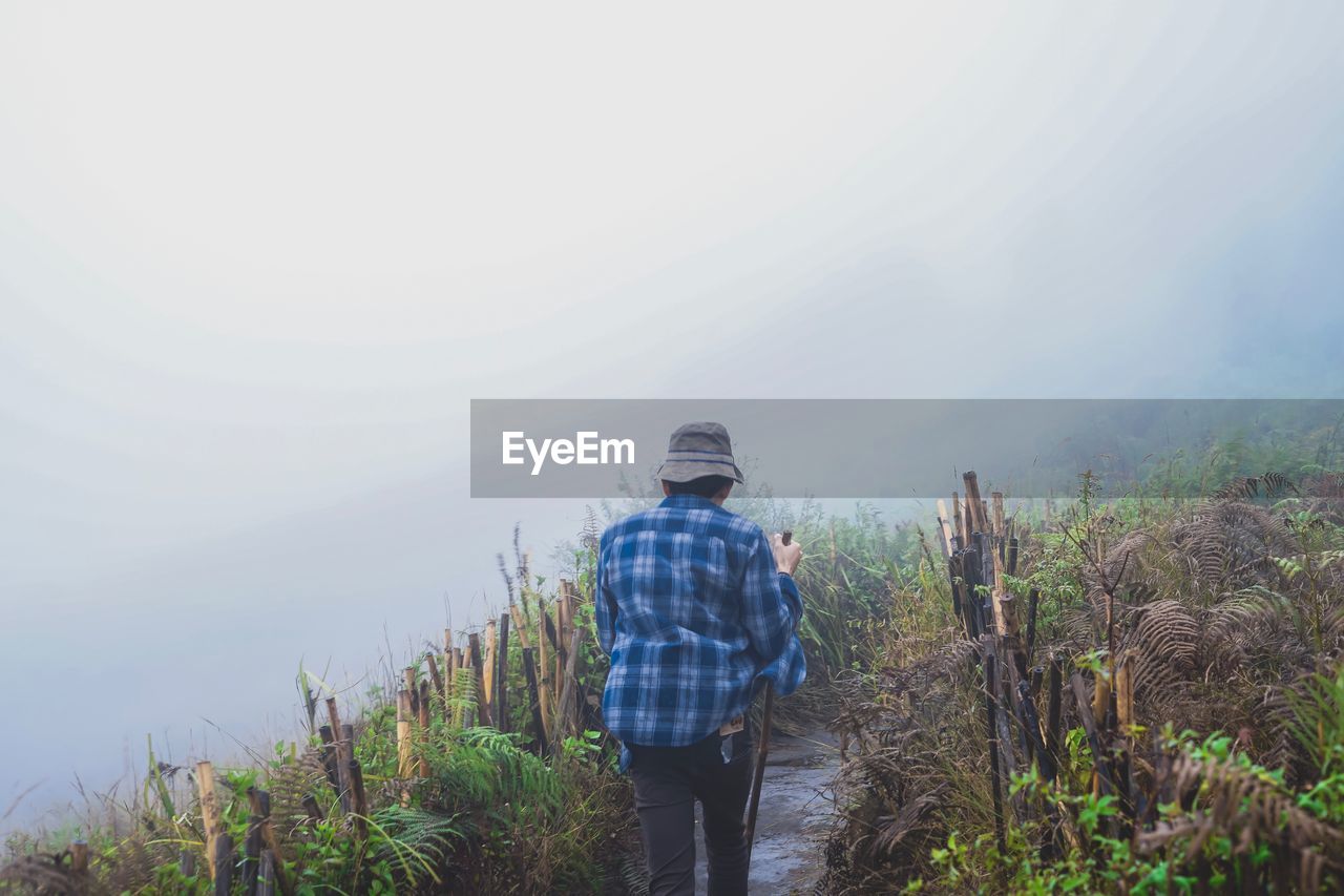 Rear view of man walking on mountain during foggy weather