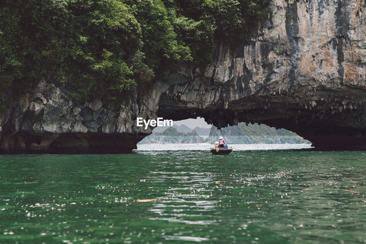 People rowing boat on halong bay under rock formation