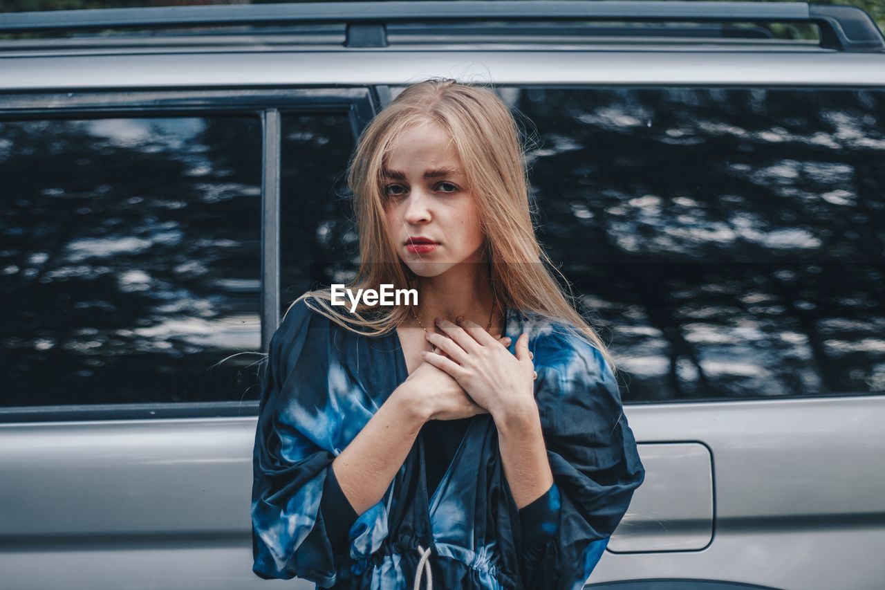 Portrait of beautiful young woman standing against car