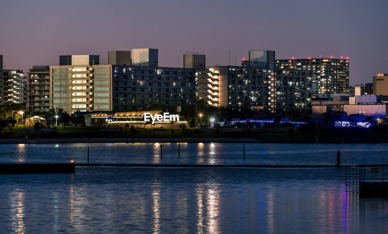 Illuminated buildings by river against sky in city at night