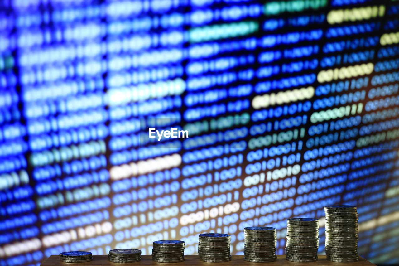 Stacked coins against binary code on screen