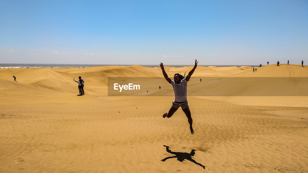 Man jumping on sand against sky at beach