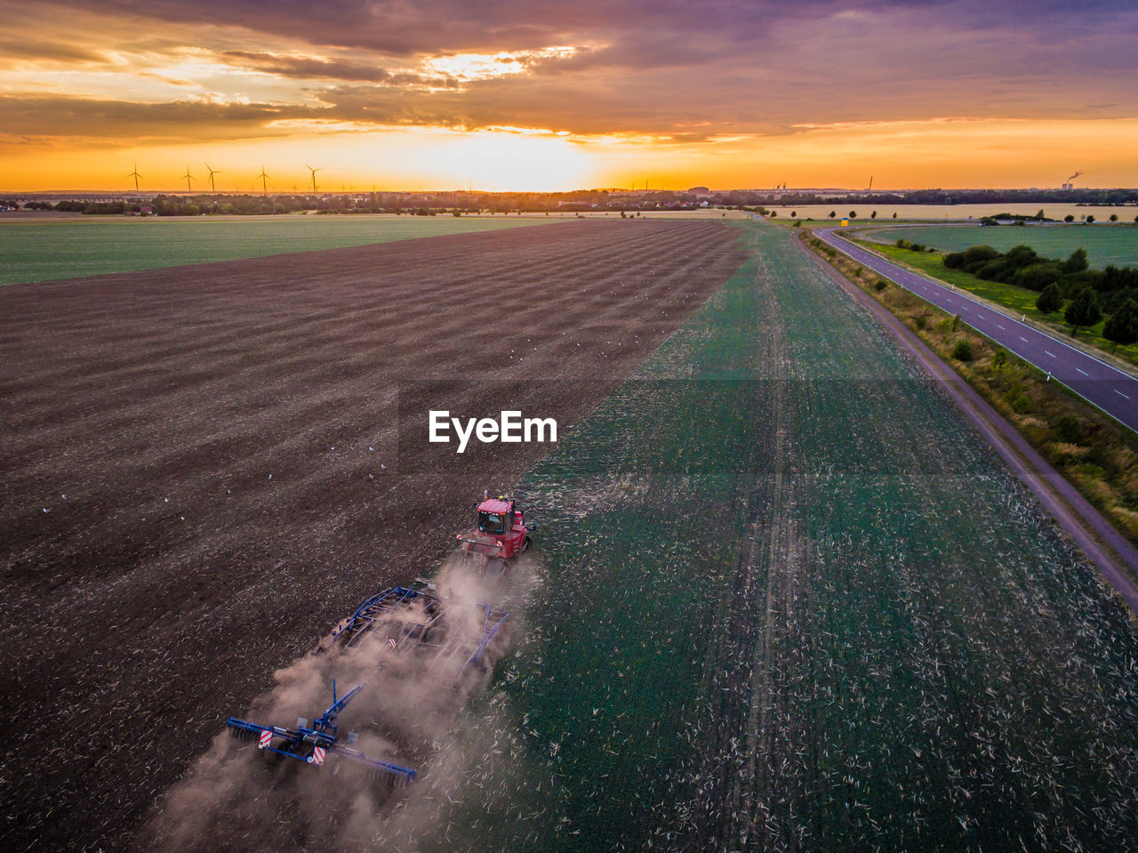 High angle view of combine harvester on field against sky during sunset