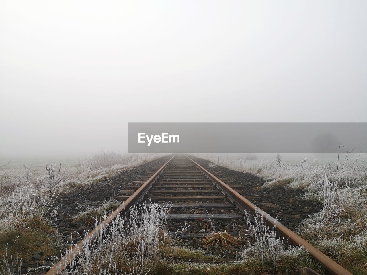 Railroad tracks on field against sky during winter