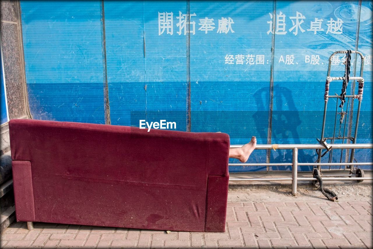 Low section of person relaxing on red sofa against blue wall