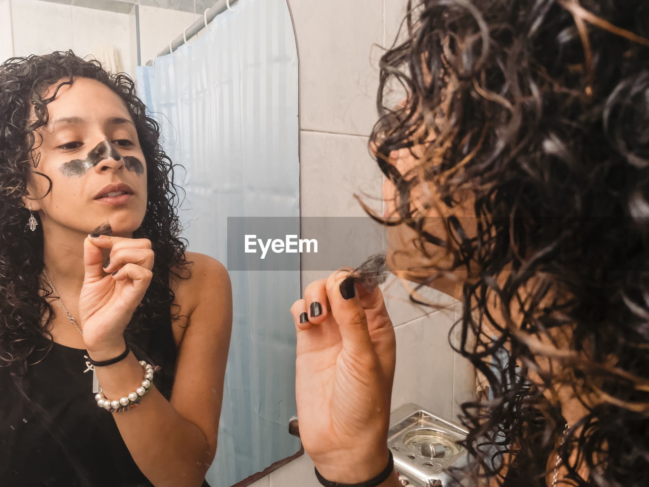 Woman peeling off black facial mask of her face in the bathroom.