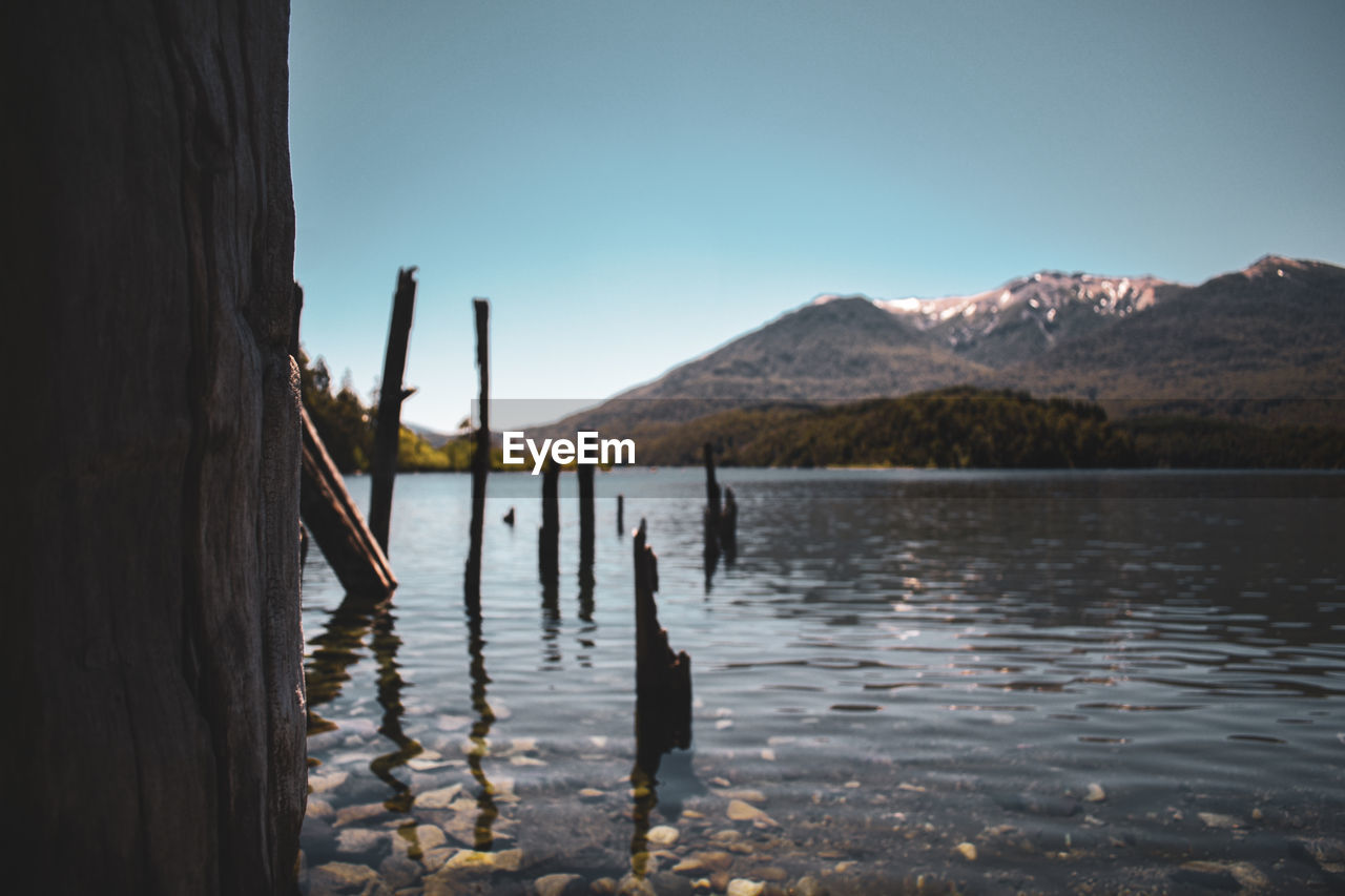WOODEN POSTS IN LAKE AGAINST MOUNTAINS
