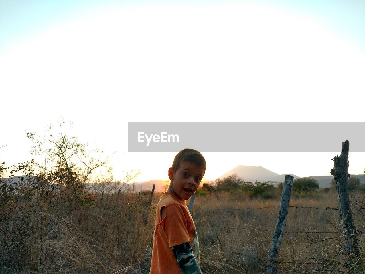 Portrait of boy standing on field against clear sky during sunset