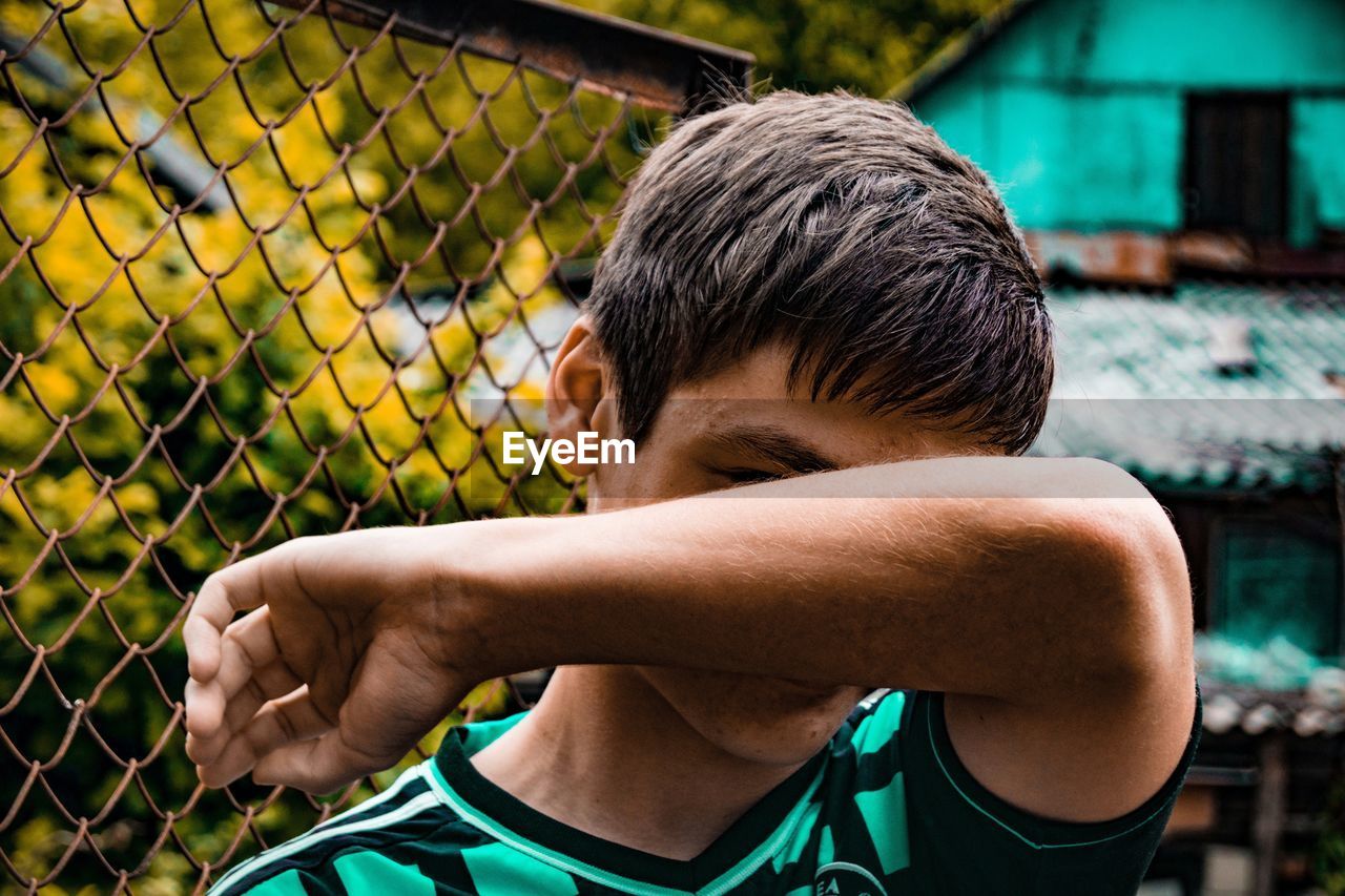 Teenage boy hiding face against fence