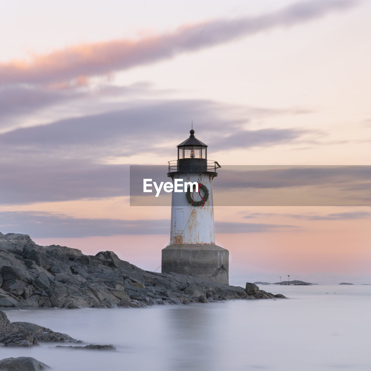 Lighthouse by sea against sky during sunset