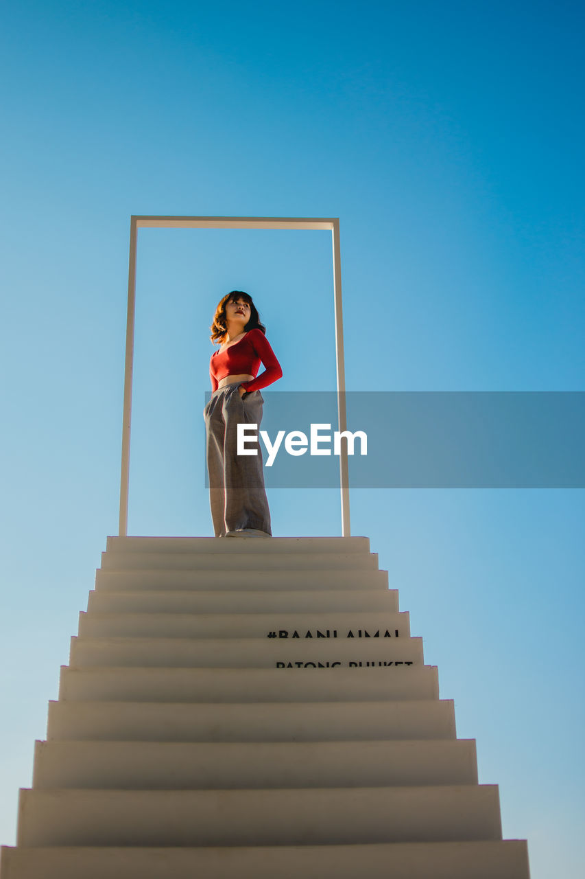 LOW ANGLE VIEW OF YOUNG WOMAN STANDING ON STAIRCASE