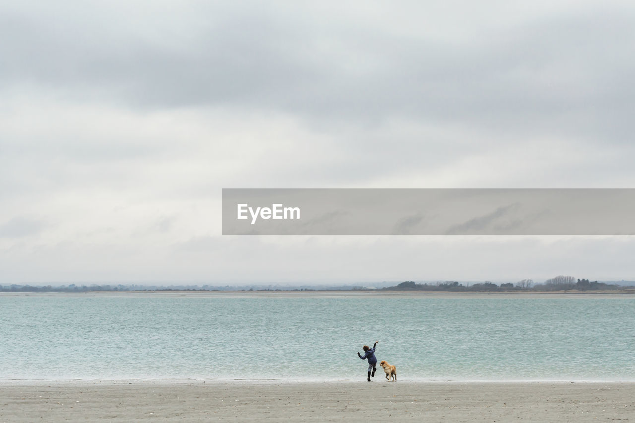 Boy throwing pebbles into the sea with dog on beach