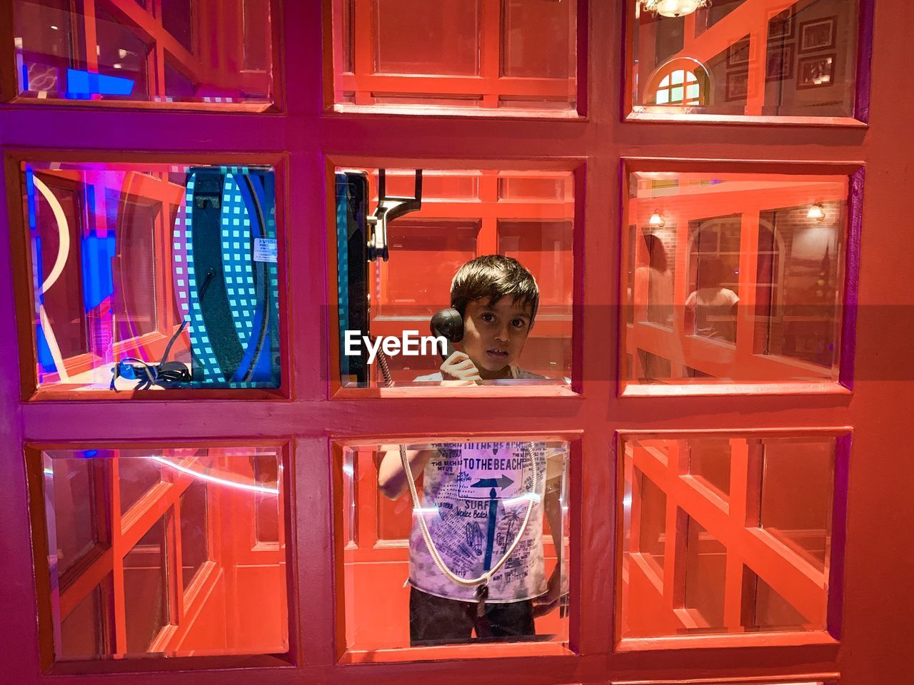 Portrait of boy talking while standing in illuminated telephone booth