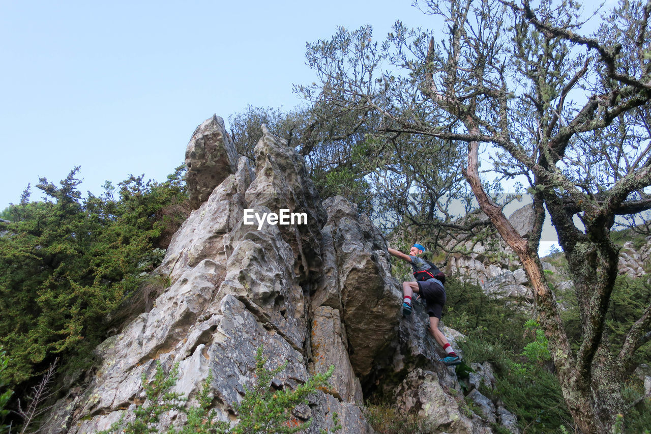 LOW ANGLE VIEW OF MAN ON ROCK AGAINST SKY