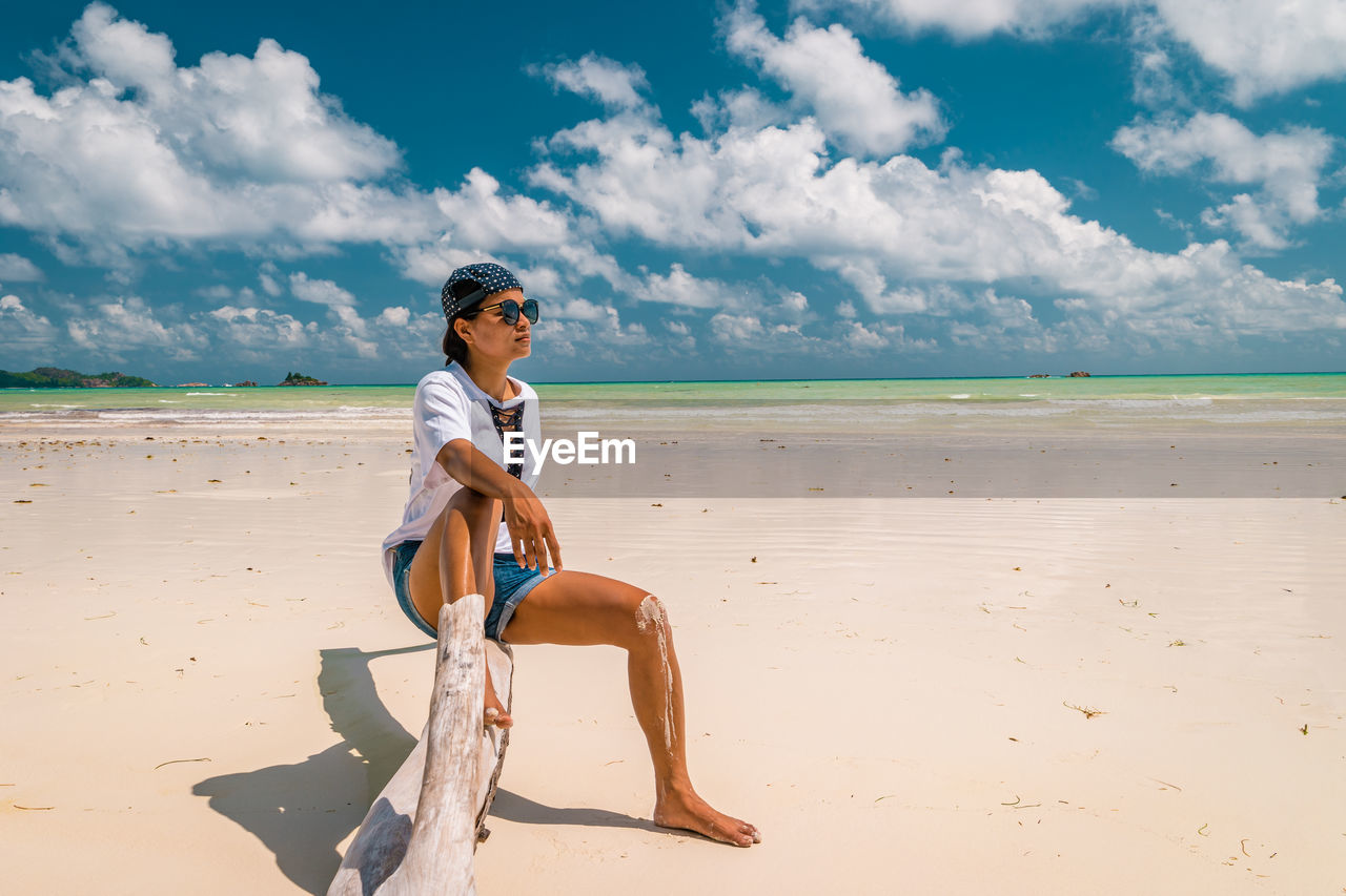 Full length of woman sitting at beach against sky