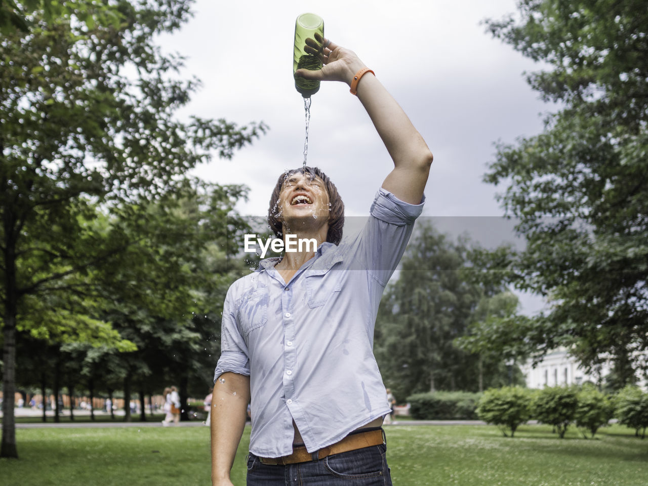 Smiling man pouring water on face at park