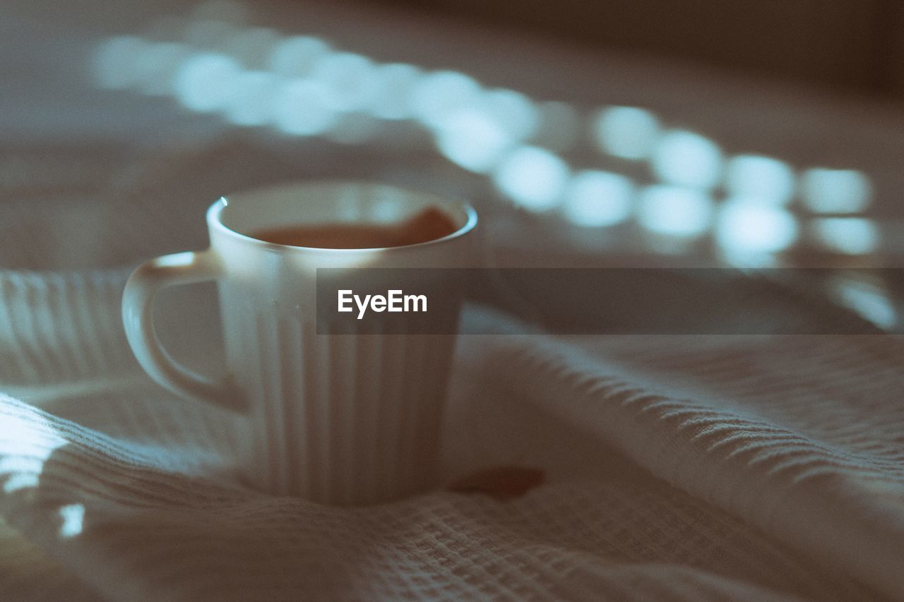 CLOSE-UP OF COFFEE CUP ON BED WITH TABLE