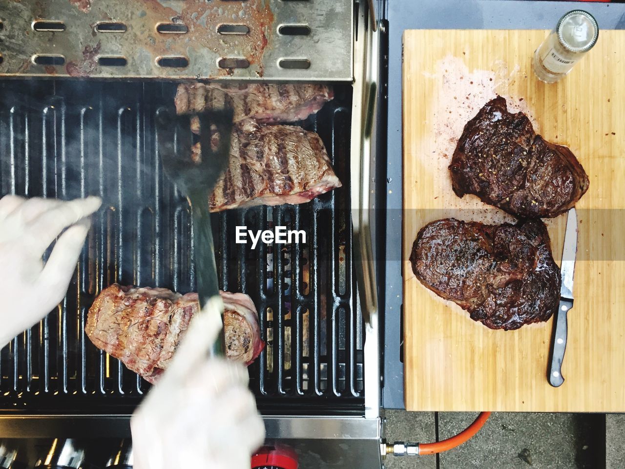 Cropped hands of person preparing steaks on barbecue