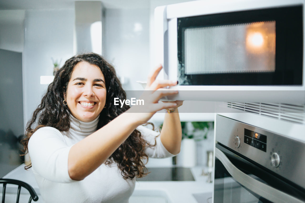 Portrait of young woman opening microwave open