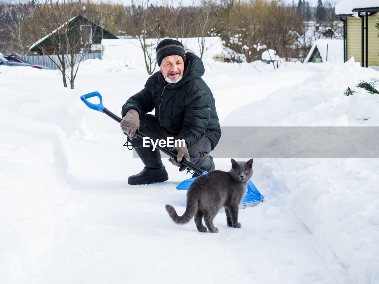 Senior man with cat crouching on snow