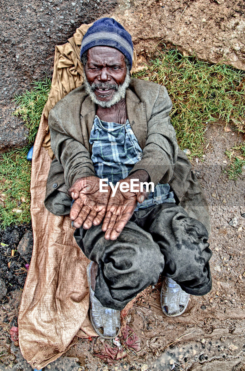 FULL LENGTH PORTRAIT OF MAN WEARING HAT SITTING OUTDOORS