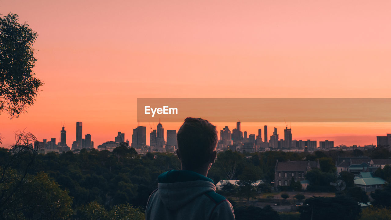 Rear view of man and buildings against sky during sunset