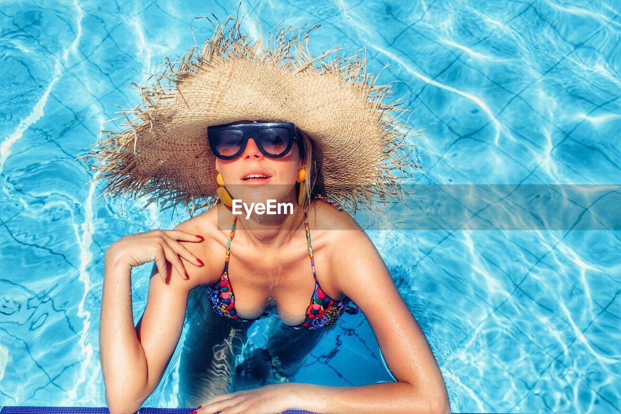 Portrait of woman wearing hat and sunglasses in swimming pool