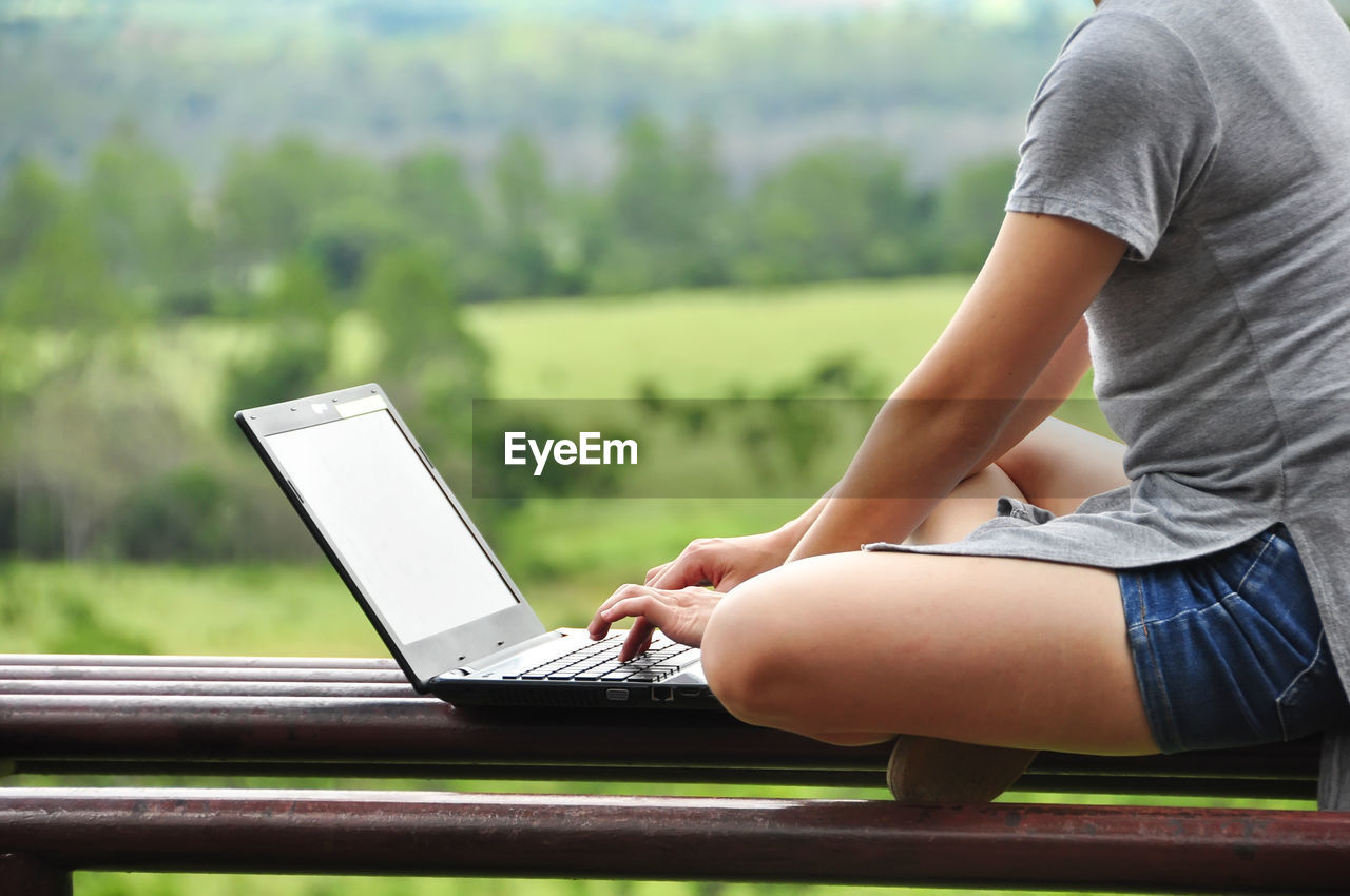 Low section of woman using laptop against landscape