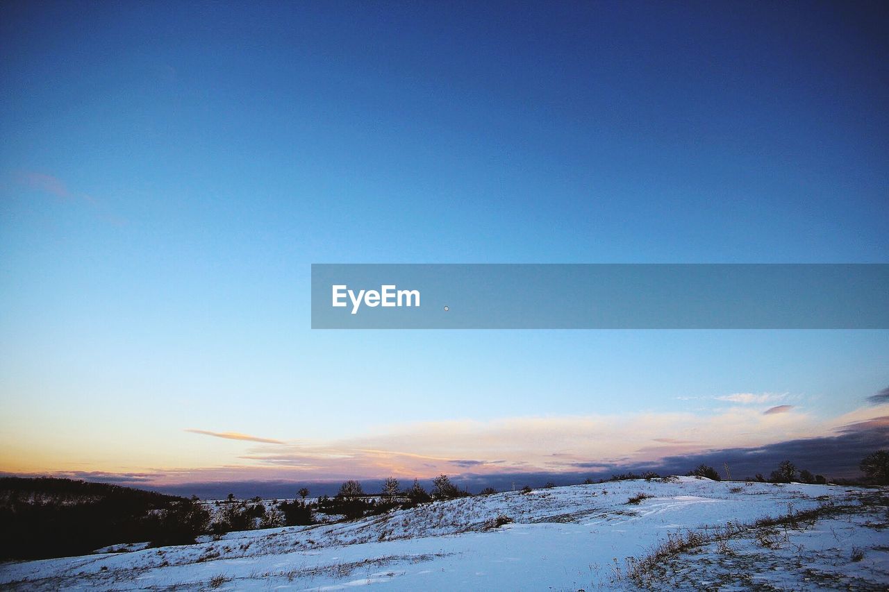 Scenic view of landscape with snow against sky during sunset