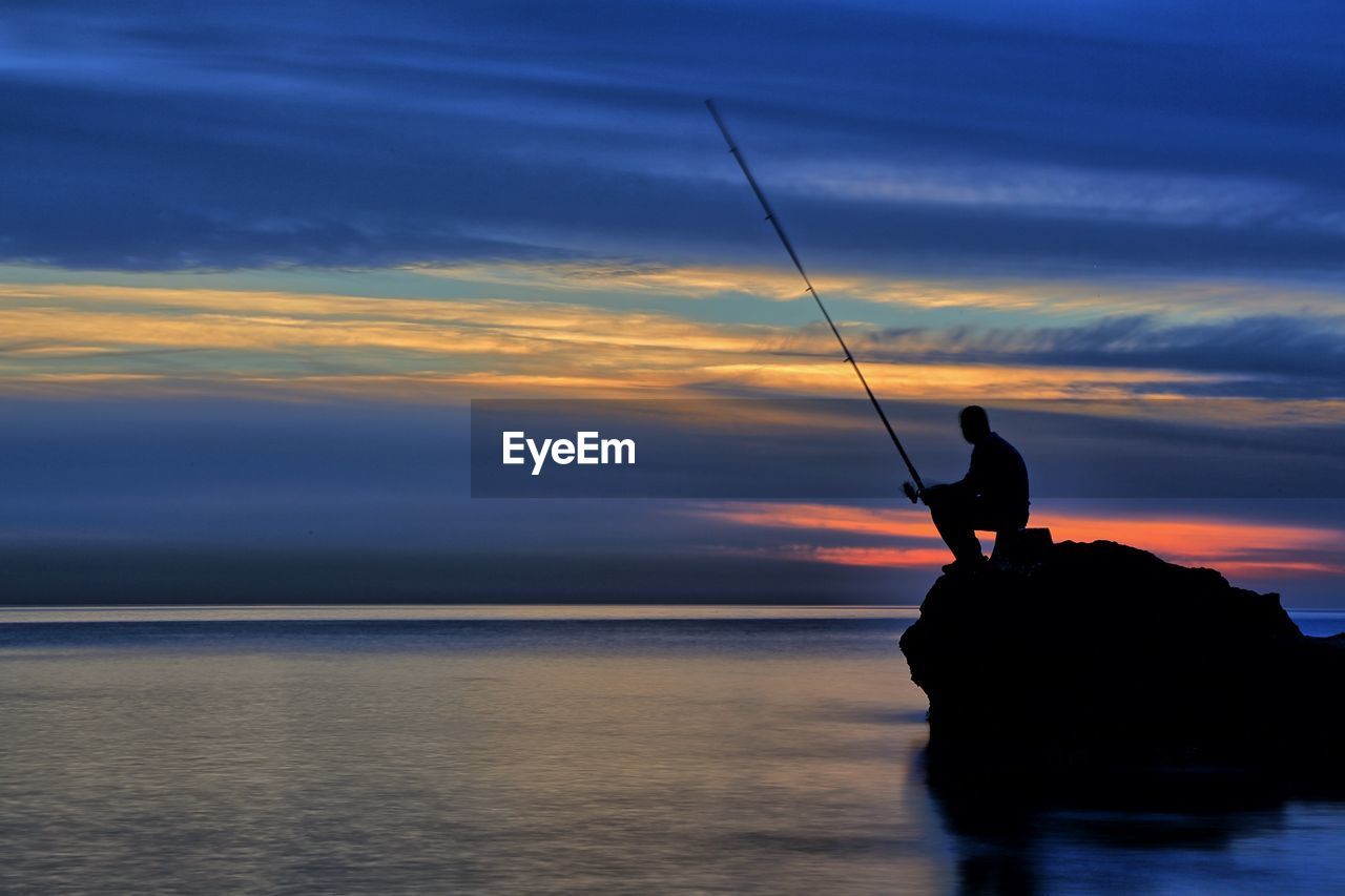 Silhouette man fishing in sea against sky during sunset