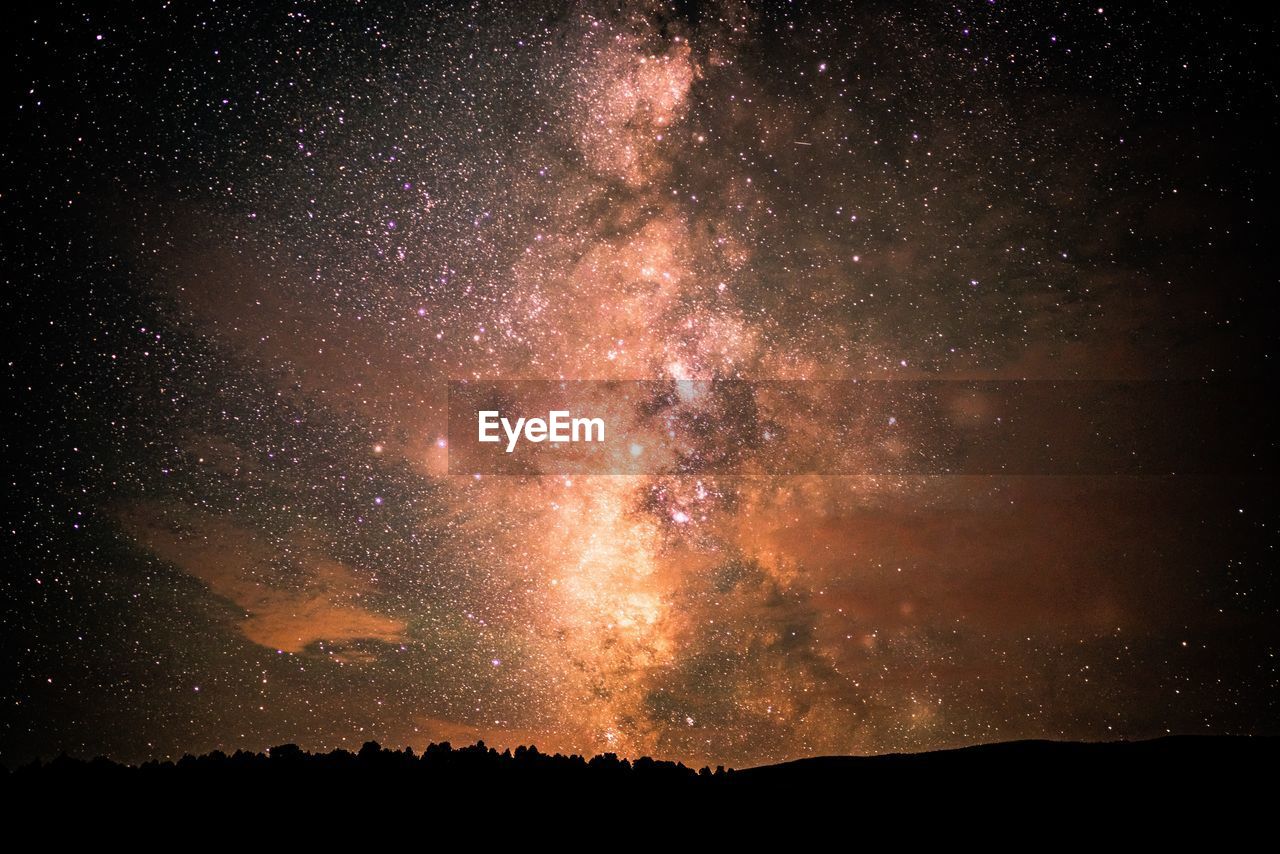 FIREWORK DISPLAY ON SILHOUETTE LANDSCAPE AGAINST STAR FIELD