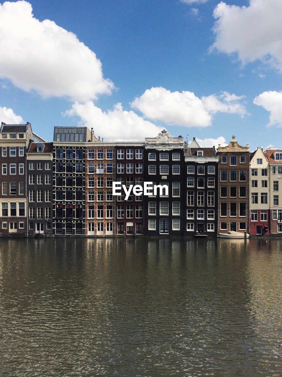 Buildings by lake against cloudy sky